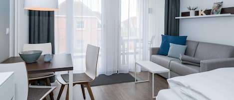 Wohn-Ess-Schlafbereich mit Sofa, Esstisch, Sitzgelegenheit und Doppelbett sowie Zugang zum Balkon