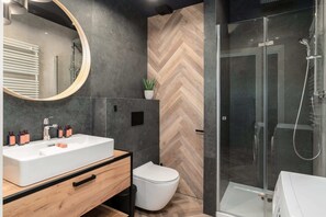 A sleek bathroom featuring a round mirror, a white sink, and a walk-in shower.