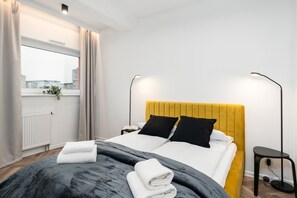 A cozy bedroom featuring a yellow upholstered headboard, two black pillows, and a bedside lamp.