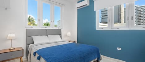 Wake up refreshed in this bright and airy room, featuring a comfortable bed adorned with a vibrant blue throw, set against the backdrop of a calming teal wall.