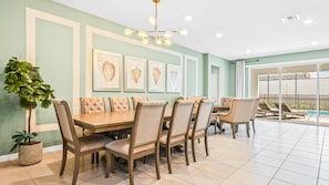 Elegant dining room with seating for 14, chic wall art, modern chandelier, and poolside views.