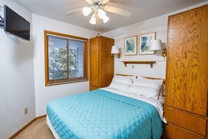 Primary bedroom (main level) includes a queen bed, ceiling fan, TV, room darkening shades, hangers and extra blankets