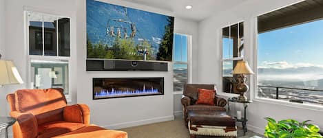 Living Room: "Cozy ambiance with electric fireplace, sofa chairs, and natural light."