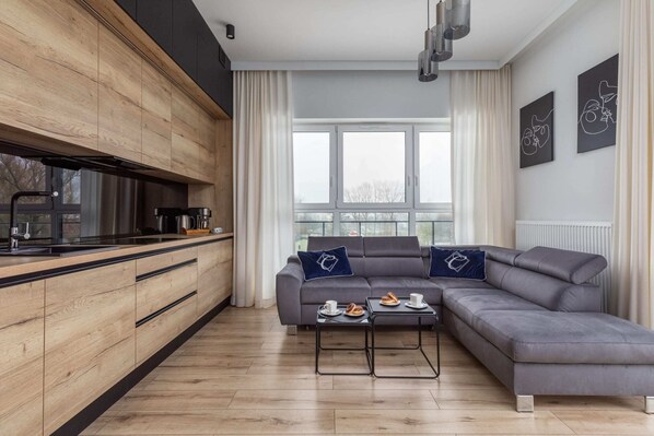 A contemporary living space featuring a wooden kitchenette, a gray sofa, and a dining area.