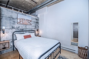 Cozy loft bedroom with a simulated concrete accent wall, vintage touches, and a comfortable queen bed