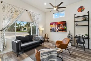 Living room has a sofa, two lounge chairs, writing desk & 75 inch smart TV.