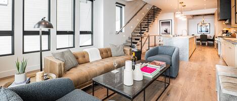 Main Level Living Room with contemporary leather sofa, plush arm chairs, elongated gas fireplace, and a 65” Smart TV, and access to one of the private decks