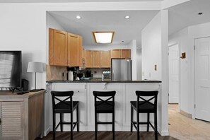 The kitchen is connected to the living room over the kitchen bar which features three bar stools. The kitchen includes stainless steel appliances, ample counter space, and all the basic appliances and cookware to prepare a delicious meal.