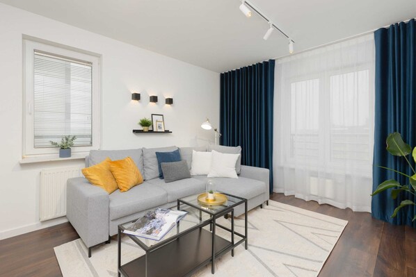 A cozy living room with modern gray furniture, accented by yellow cushions and blue curtains.
