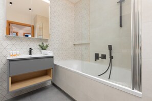 A modern bathroom with a bathtub, wooden accents, and mosaic tiles.

