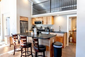 The fully equipped kitchen is a bright and modern space complete with stainless steel appliances, ample cabinet and counter space, classic wood finishes, and a large kitchen island with three barstools.