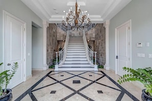 Grand Staircase - - Make an unforgettable entrance through this grand foyer featuring a sweeping dual staircase and ornate chandelier
- Marble floors with geometric inlay add elegance and style
- Regal welcome sets the tone for your beachfront escape