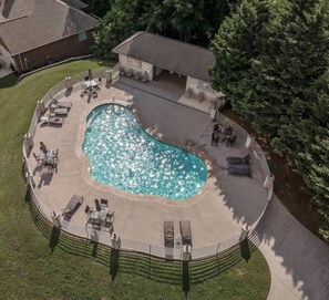 A stunning aerial view showcases the community pool's sparkling waters and ample seating areas, just steps from the house