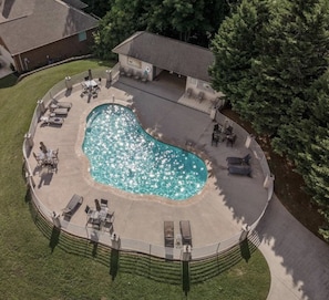 A stunning aerial view showcases the community pool's sparkling waters and ample seating areas, just steps from the house