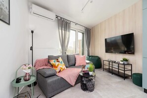 A bright living room with a sofa, TV, and dining table, decorated with green accents.
