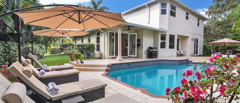 Escape to your own private oasis with a heated pool and loungers surrounded by lush greens in the backyard. Perfect for relaxing and soaking up the sun!