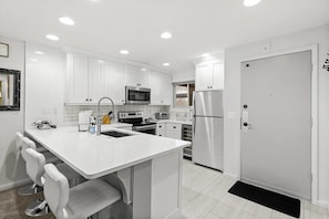The fully equipped kitchen features stainless steel appliances, all-white cabinets and countertops, and seating for four at the spacious kitchen bar.