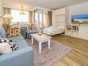 Wohnzimmer mit Sofa, Schrankbett (ausgeklappt) und TV