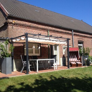 Terrasse mit Sitzmöbeln, Sonnenmarkise, Strandkorb und Grill am großen Garten