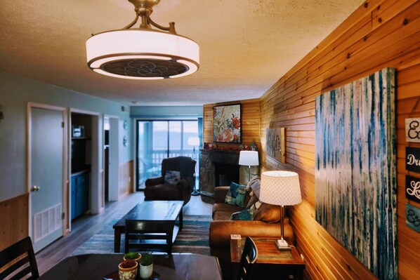 View of living space from kitchen bar shows a table for 4, leather sofa and recliner, fireplace, TV and view of mountains from balcony