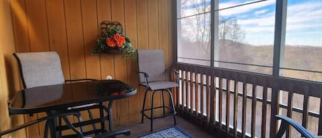 The screened-in balcony provides a beautiful view of the mountains with plenty of seating and a cafe table