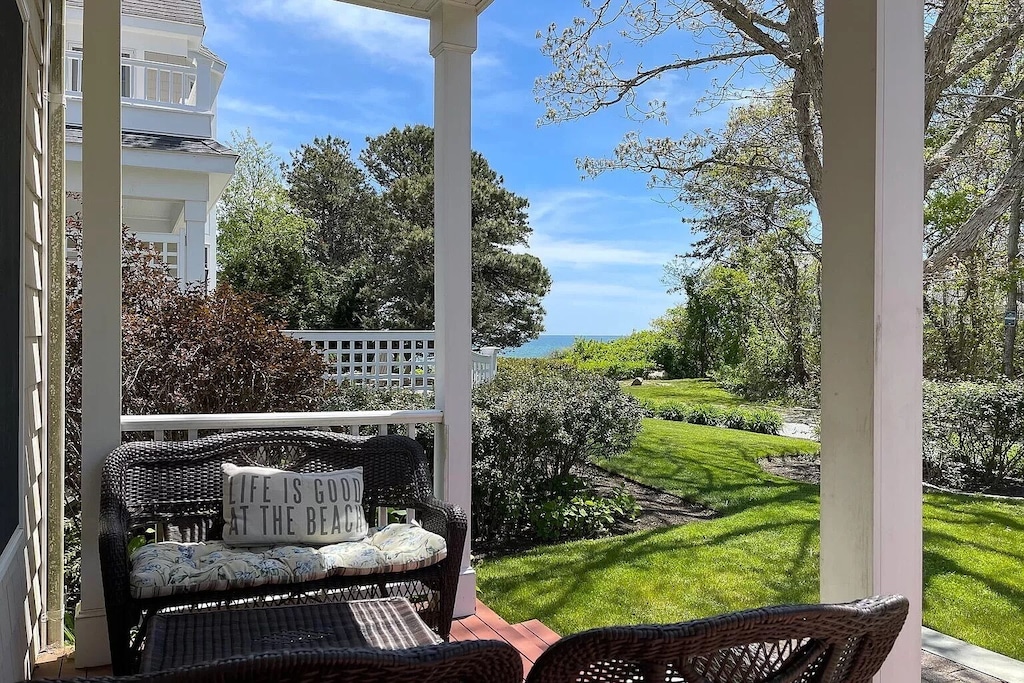 A vacation rental in Cape Cod has a roomy porch with wicker furniture with the ocean just a few hundred feet beyond