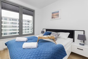 Cozy bedroom with a large bed featuring a blue throw and white linens, complemented by floor-to-ceiling windows.