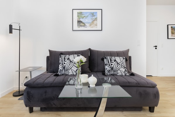 Bright and modern living room with a comfortable gray sofa, light wood floors, and minimalist decor.