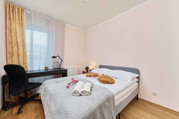 A cozy bedroom with a double bed, a blanket laid out neatly, and natural light coming in from the window.
