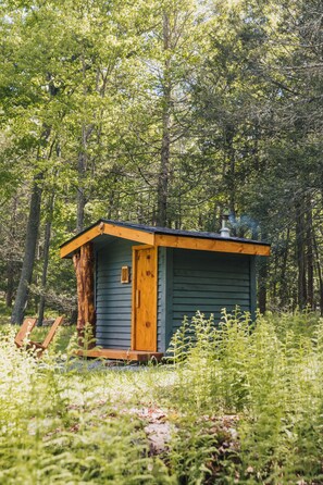 Custom wood-burning sauna with built-in seating, perfect for relaxing after a day out. A large window looks out into the trees, blending cozy warmth with a peaceful woodland view. A serene spot to unwind and recharge.