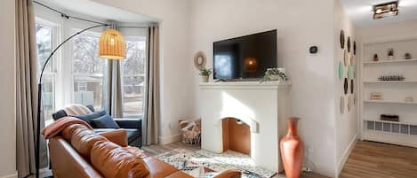 Bright and cozy living room with 55" Smart TV, nonfunctional fireplace,  leather sofa and bay windows