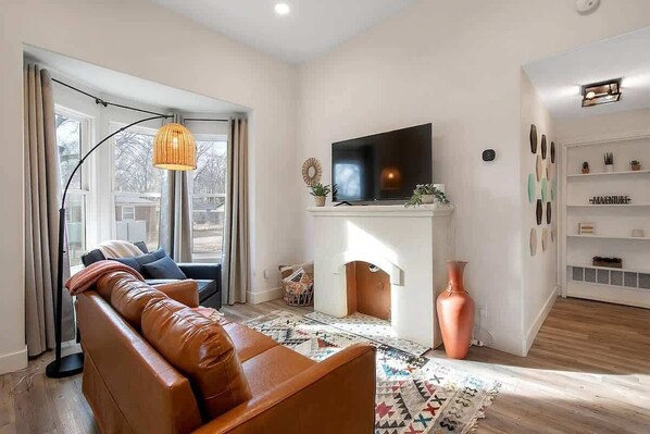Bright and cozy living room with 55" Smart TV, nonfunctional fireplace,  leather sofa and bay windows