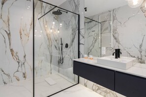 Luxurious bathroom with marble walls, a glass-enclosed shower, and a sleek vanity area with a large mirror.

