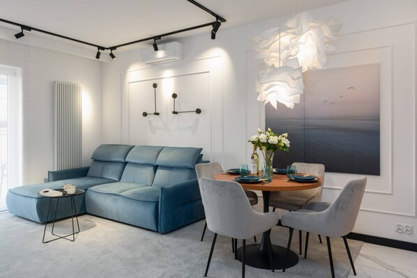 Stylish living room with a blue sofa, modern decor, and a round dining table accompanied by elegant chairs.

