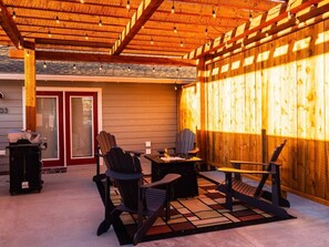 Private patio with pergola, lighting, Adirondack chairs, fire table and grill.