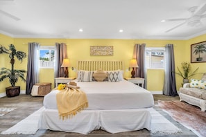 Tropical-style master bedroom with sunny yellow tones, a pull-out sofa, large smart tv, and an en-suite bathroom.