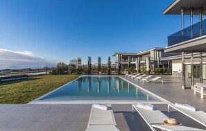 Spacious paved terrace with a large private pool with a built-in waterfall, surrounded by sun loungers, parasols and outdoor dining tables and seating
