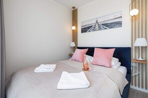 A cozy bedroom with a pink and white color palette, a double bed, and modern lighting.