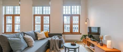The living room is warmly furnished and spacious, and it has an outside view of the Grand Market of Antwerp.