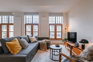 The living room is warmly furnished and spacious, and it has an outside view of the Grand Market of Antwerp.