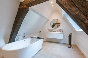 Modern bathroom with wooden beam constructions is a spacious and well-lit room with plenty of natural light. It has a large bathtub and a walk-in rain shower with marble touches.