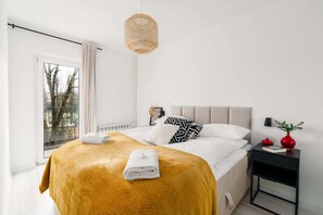 A cozy bedroom featuring a comfortable bed with a mustard throw blanket, accented by natural light.

