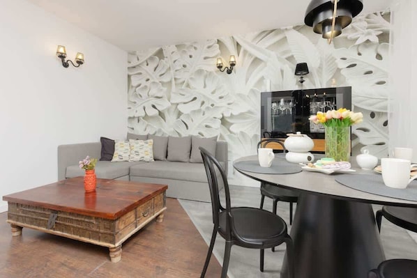 A stylish living room with a gray sofa, a rustic wooden coffee table, and a dining area with elegant black chairs.