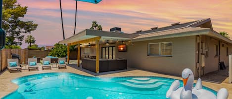 Large backyard with pool, outdoor dining table, outdoor lounging area, putting green, BBQ, cornhole, sun loungers, and fire pit area.