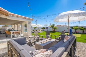 Enjoy ultimate relaxation in this chic outdoor lounge with plush seating, a fire table, and string lights for the perfect ambiance.