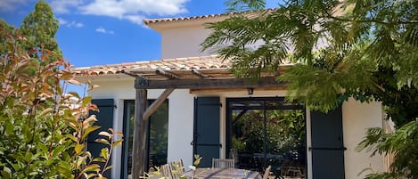 Maison avec terrasse couverte, jardin abrité par végétation et brise vue