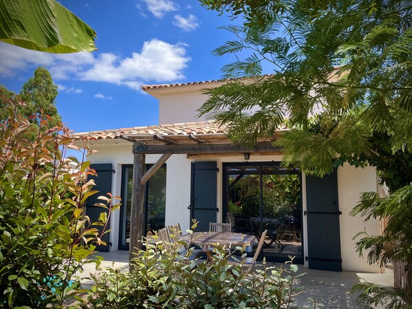 Maison avec terrasse couverte, jardin abrité par végétation et brise vue