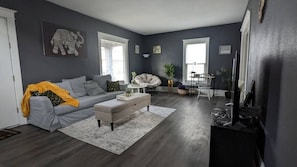 The living room has a sofa bed, papasan chair and a computer desk with lamp, and 50+inch Smart TV.