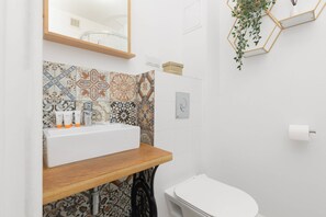 A compact bathroom with colorful patterned tiles, a wooden countertop, and minimalist decor.
