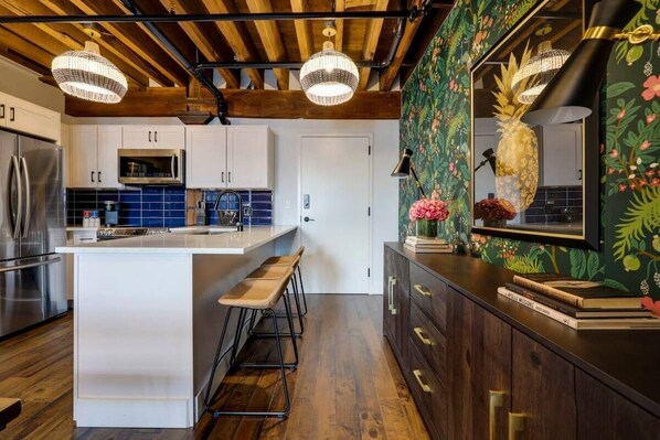 🌴 Welcome to paradise in the kitchen! Transform your cooking space into a tropical oasis with this vibrant wallpaper and charming wooden bar stools. #TropicalVibes